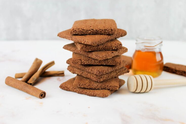 stack of healthy chocolate graham crackers sits beside cinnamon sticks and a jar of honey