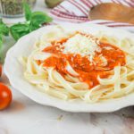 plate of noodles covered in homemade spaghetti sauce sits beside fresh tomatoes, basil and a wooden sppon