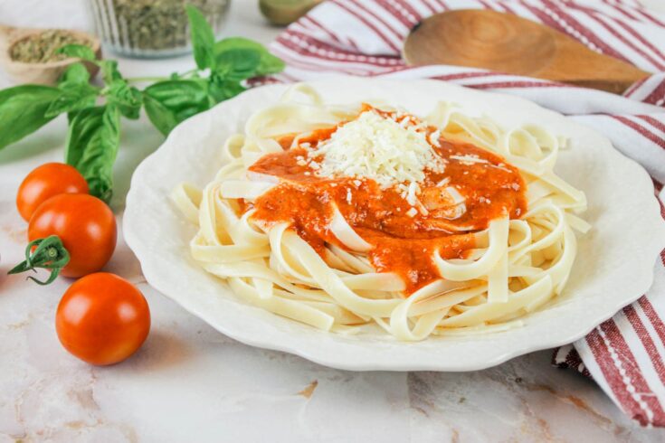 plate of noodles covered in homemade spaghetti sauce sits beside fresh tomatoes, basil and a wooden sppon
