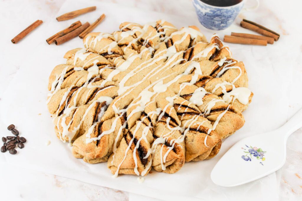 cinnamon rolls sit on a piece of parchment paper beside a cup of coffee and a serving utensil
