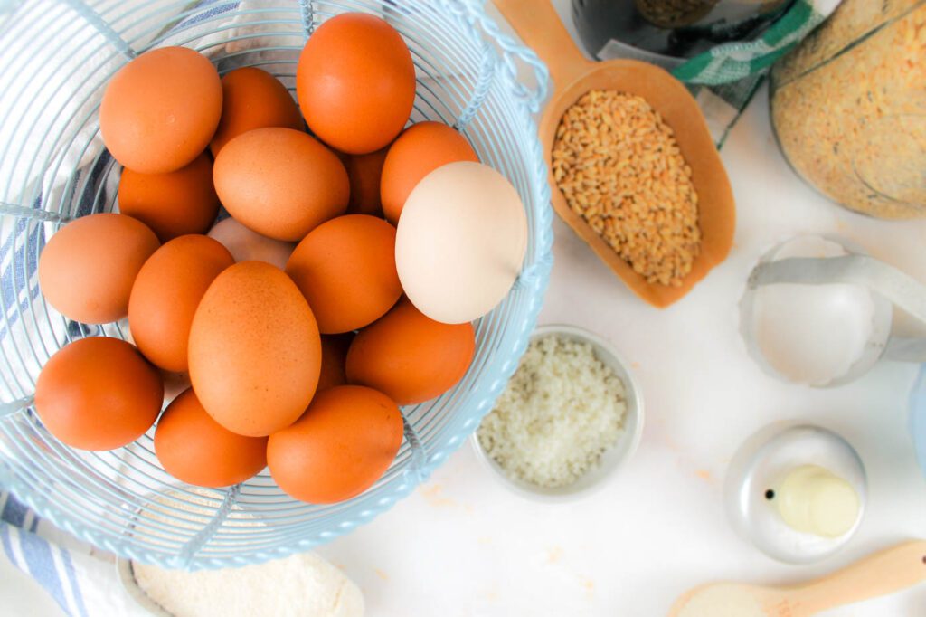 a metal basket filled with farm fresh eggs sitting besides a variety of baking ingredients and tools