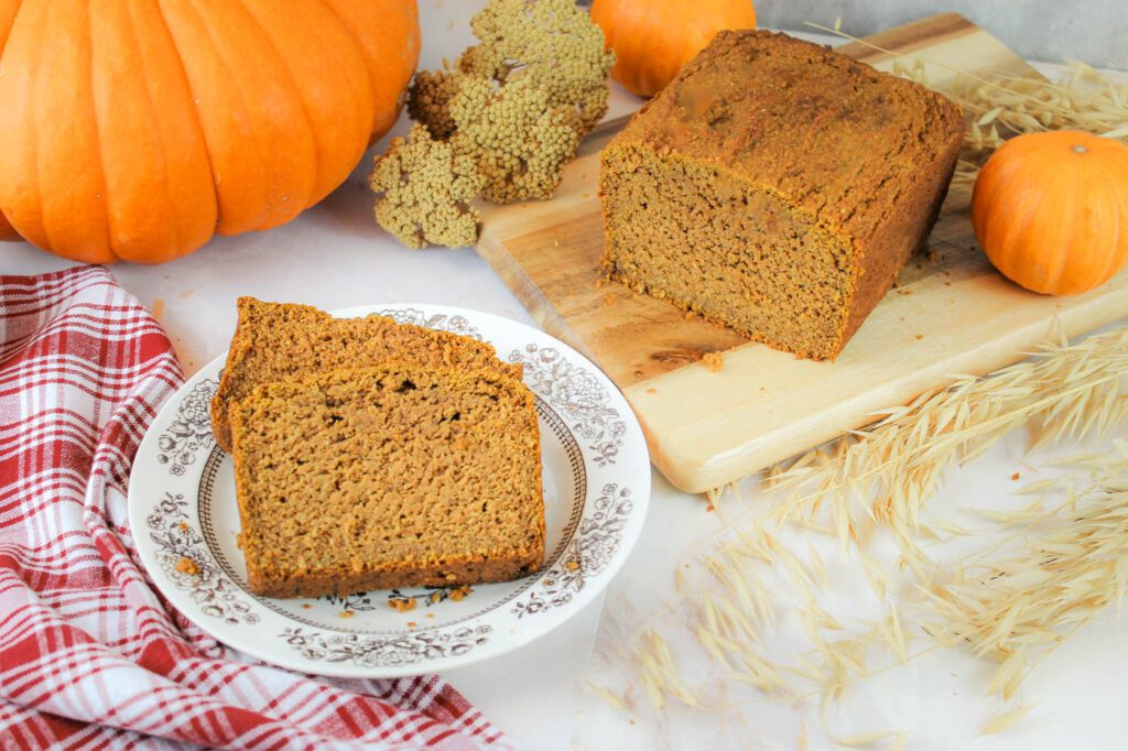a plate of pumpkin bread sits beside a loaf of bread surrounded by pumpkins and fall decor