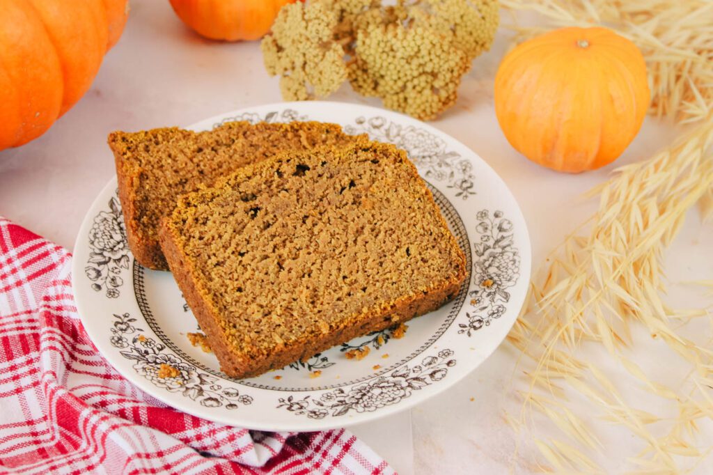 two slices of pumpkin bread sit stacked on top of each other beside some fall pumpkins and dried flowers