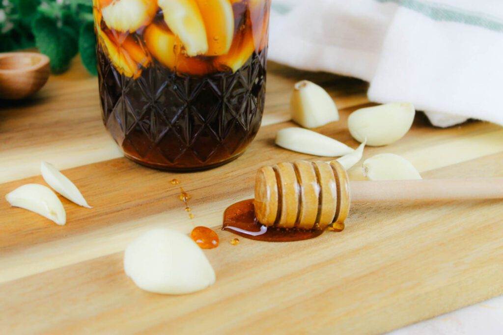 honey dipper sits beside a handful of garlic cloves on a wooden cutting board in a kitchen