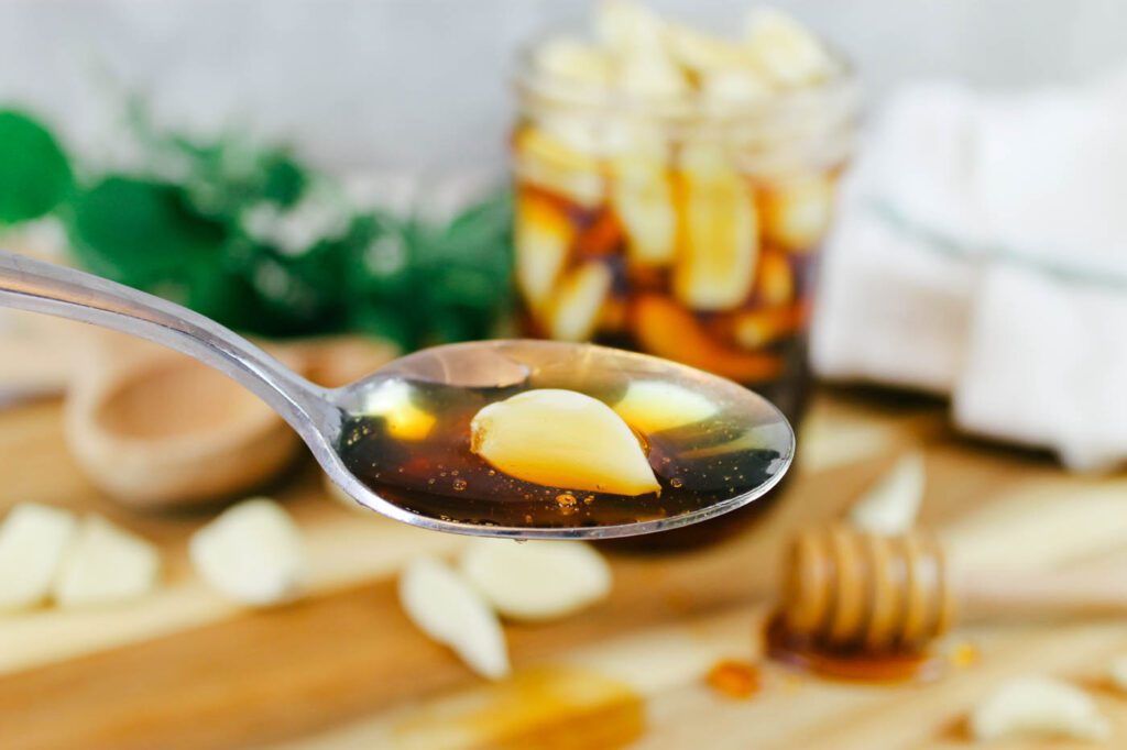 metal spoon filled with raw honey and a clove of garlic