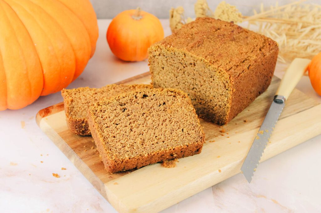 a loaf of pumpkin bread on a cutting board beside some fall decorations