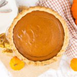 pumpkin pie with fresh milled pie crust sits on a table beside plates, forks and fresh pumpkins