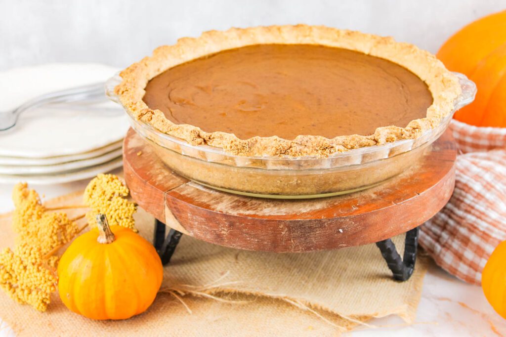 a pie sits on a wooden display stand beside some dried botanicals and pumpkins