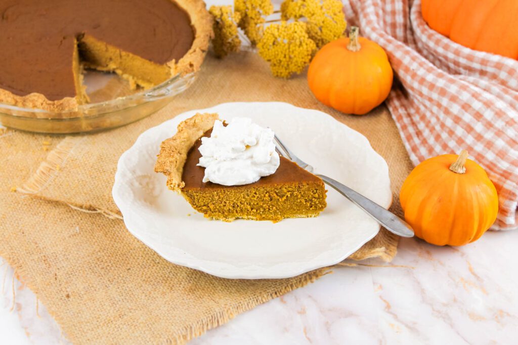 slice of pumpkin pie topped with whipped cream sits on a plate next to some fall decorations