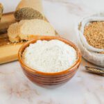 a bowl of vital wheat gluten sits next to homemade bread and a bag of wheat berries