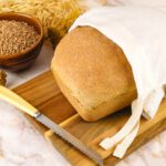 diy reusable bread bag on a cutting board next to wheat berries and dried wheat stalks