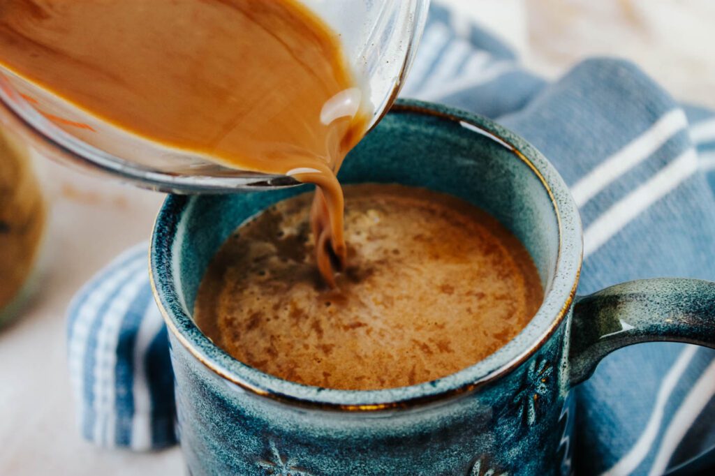 measuring cup pours hot cocoa into a blue ceramic mug