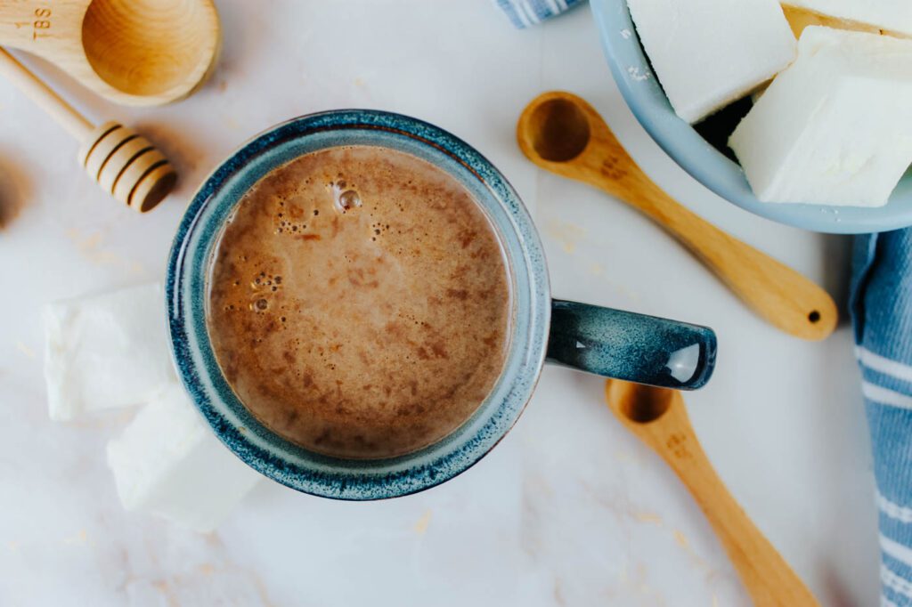 top view of a mug with hot chocolate sitting beside measuring spoons and a bowl of marshmallows 