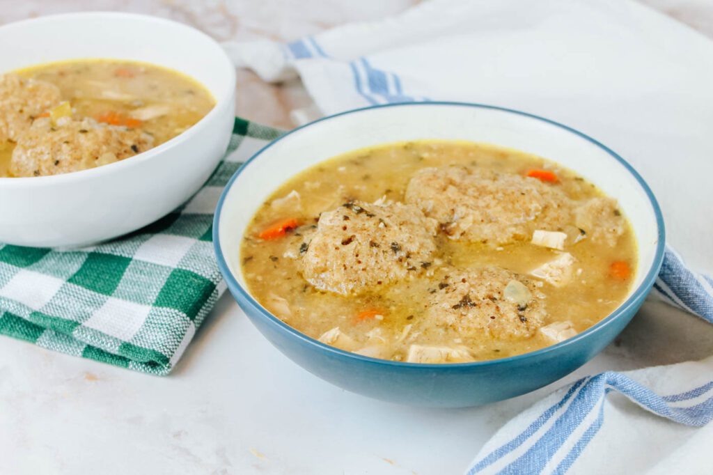 two bowls of soup sit next to a white tea towel and a green plaid kitchen towel
