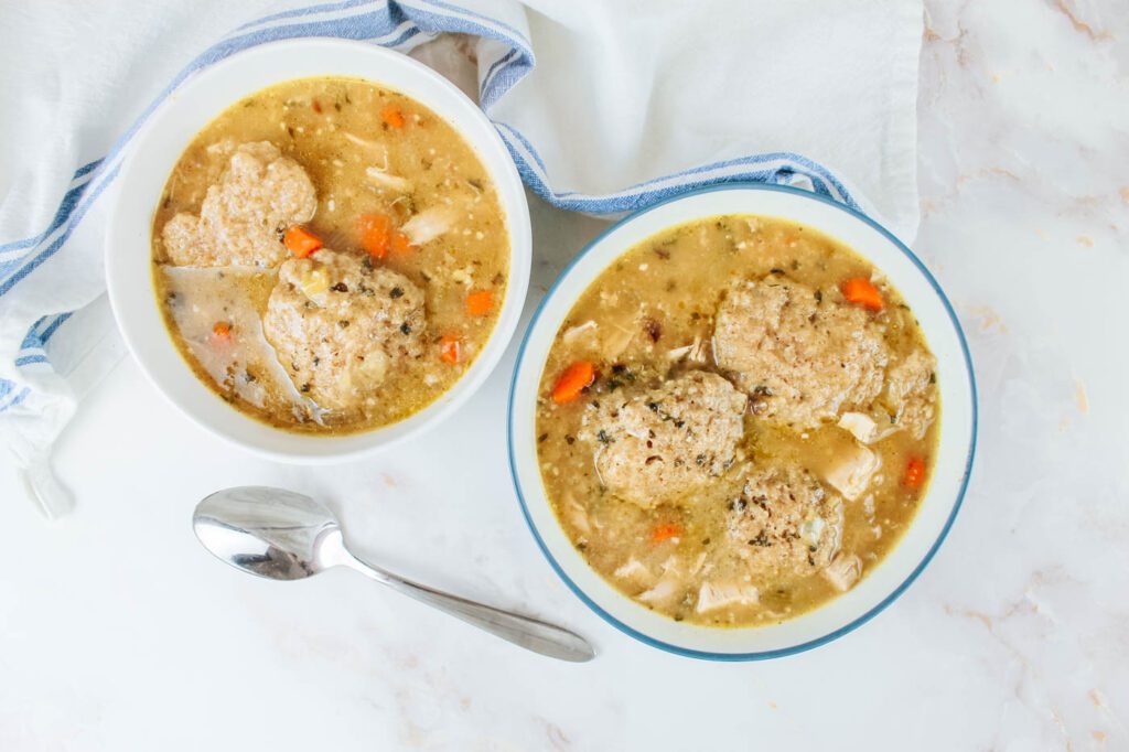 top down view of two bowls of chicken soup next to a silver spoon