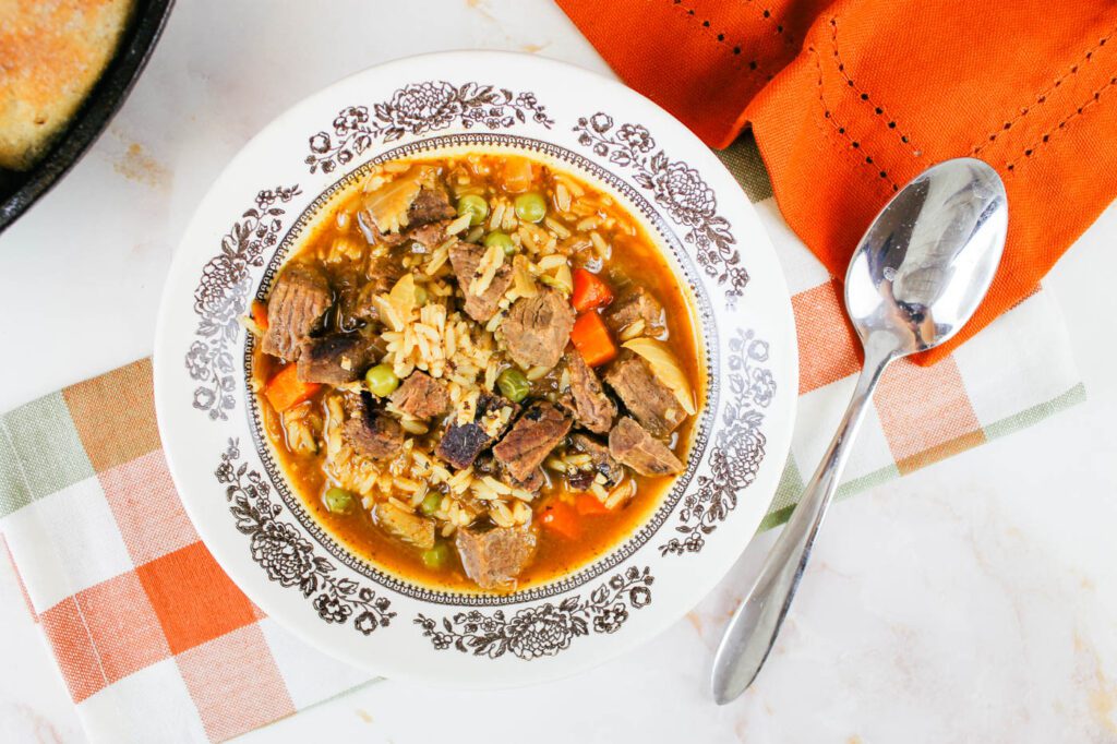 a bowl filled with easy beef and rice soup sitting next to a sliver spoon