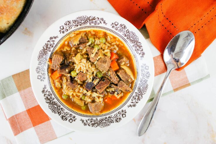 a bowl filled with easy beef and rice soup sitting next to a sliver spoon