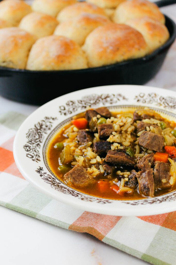 a bowl of soup sits in front of a pan of rolls