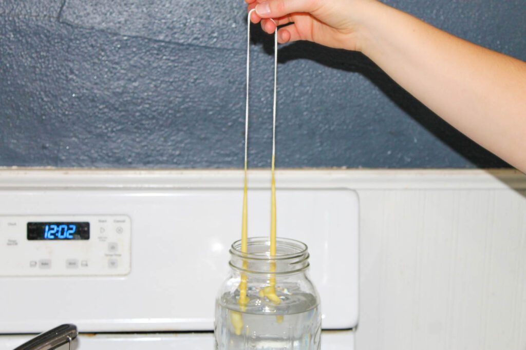 woman dips candle wick into jar of cold water
