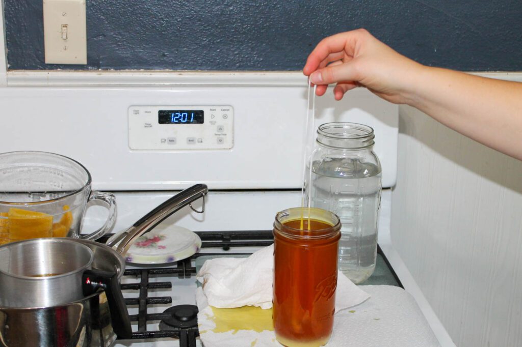 woman dips candle wick into a jar of beeswax