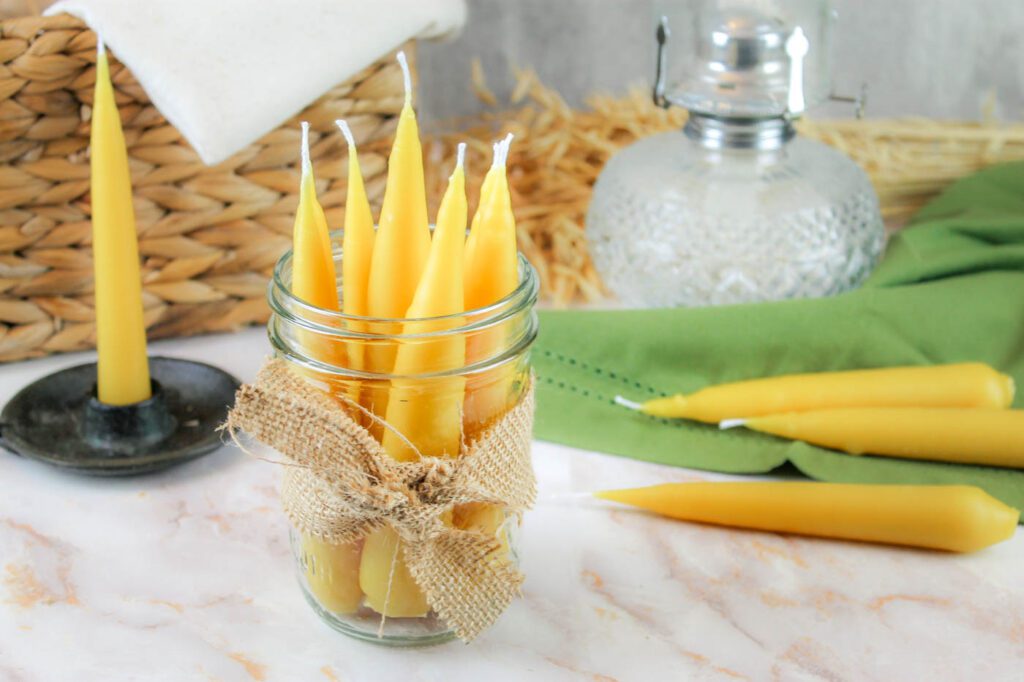 a jar of taper candles sits on a marble surface by an oil lamp and other candles