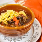 brown bowl filled with pumpkin chili recipe, topped with cheese