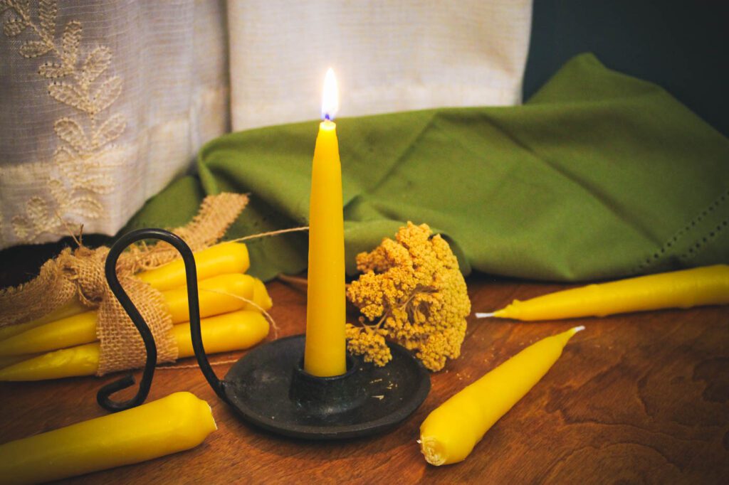 diy beeswax taper candle held by a cast iron candle holder sitting on a wood surface surrounded by homemade candles