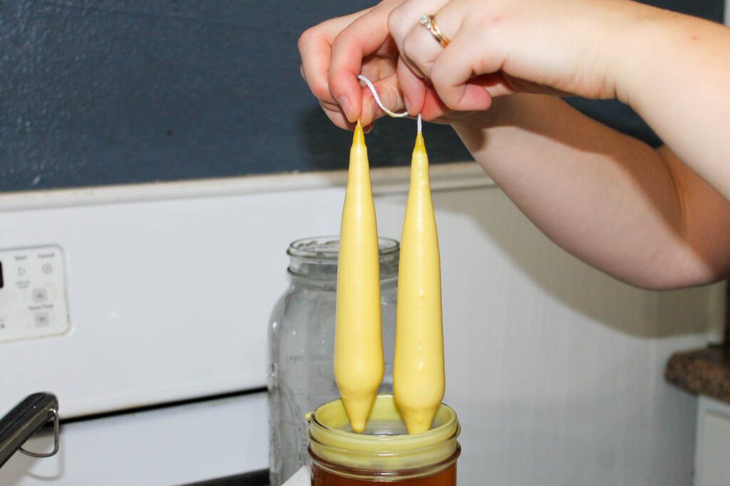 woman dips wick into hot wax to make candles