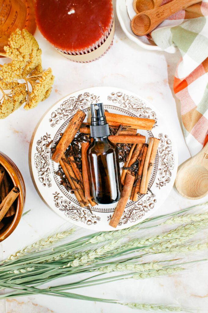 an amber spray bottle on a plate of spices surrounded by candles and dried flowers