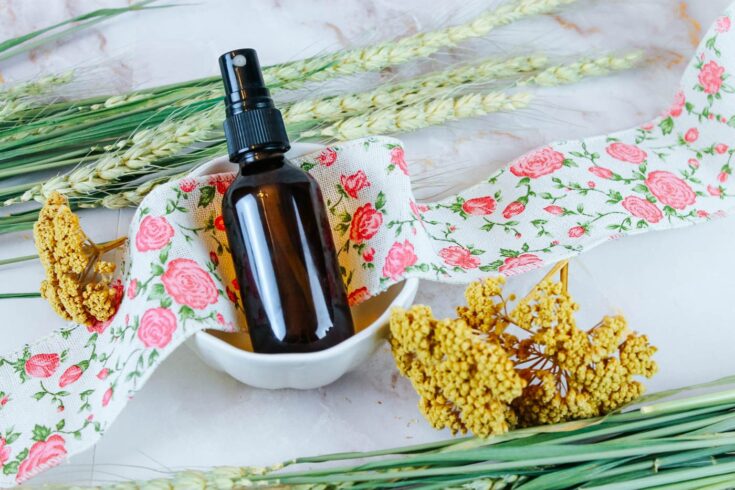 a spray bottle filled with homemade air freshener sitting on a bowl surrounded by dried botanicals