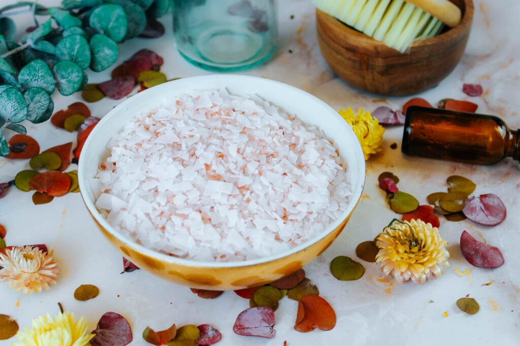 bowl filled with magnesium bath salt recipe surrounded by dried flowers and a bottle of essential oil