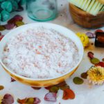 bowl filled with magnesium bath salt recipe surrounded by dried flowers and a bottle of essential oil