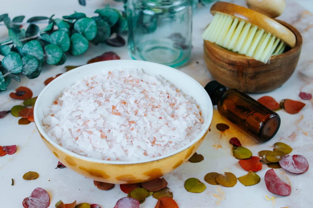 bowl filled with diy bath salt recipe for sore muscles sitting on a marble countertop beside dried herbs