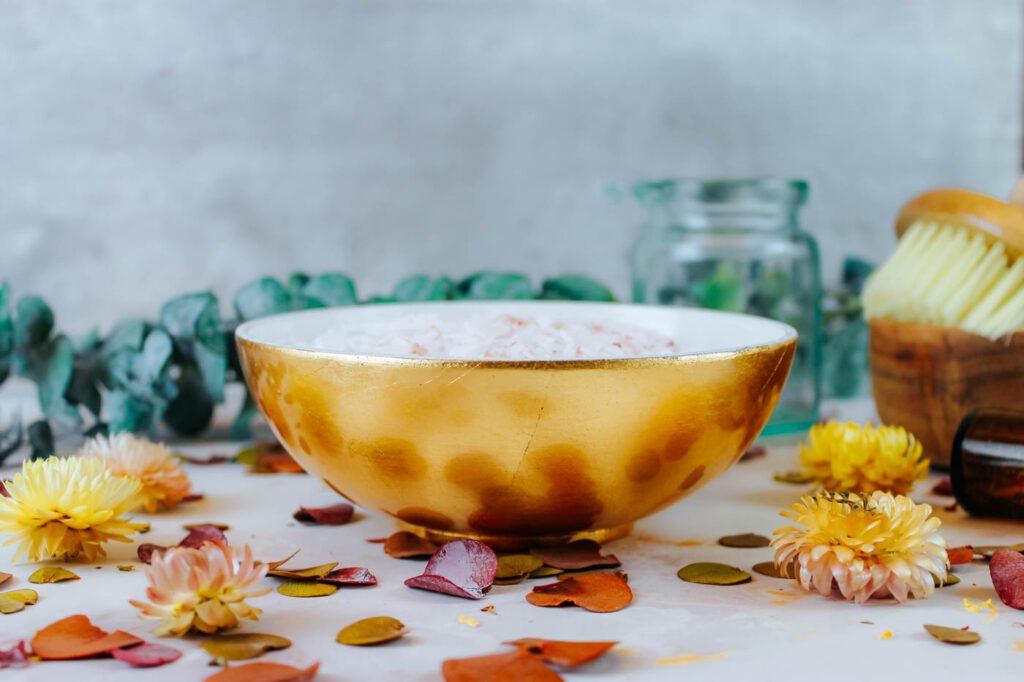 gold bowl sitting beside bath supplies and dried flowers and herbs