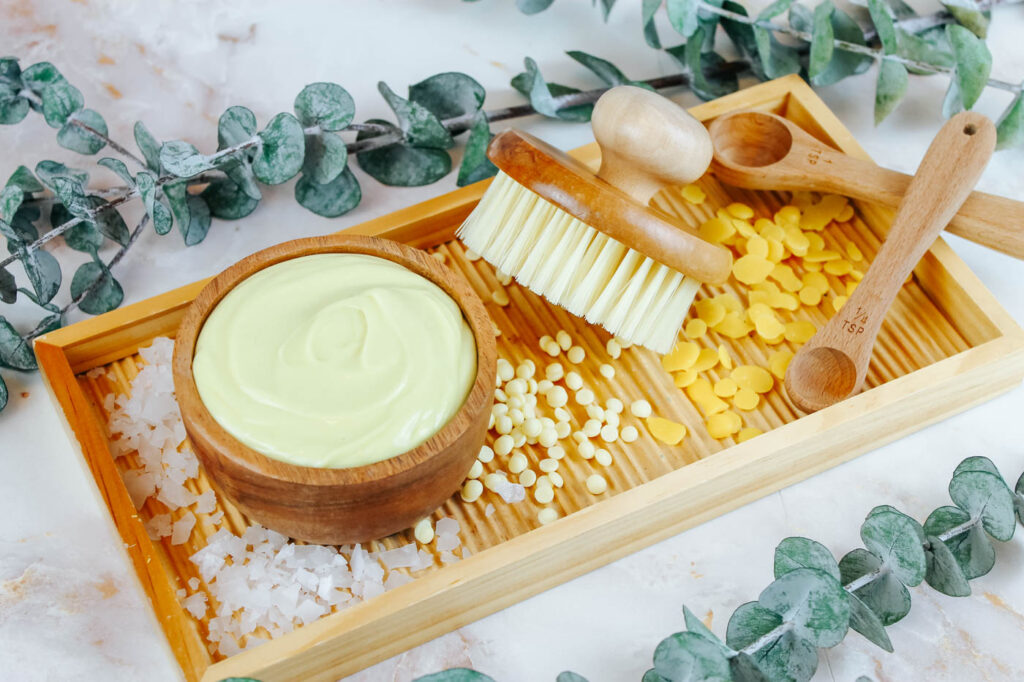 wooden tray filled with beeswax, magnesium flakes, cocoa butter and cosmetic supplies