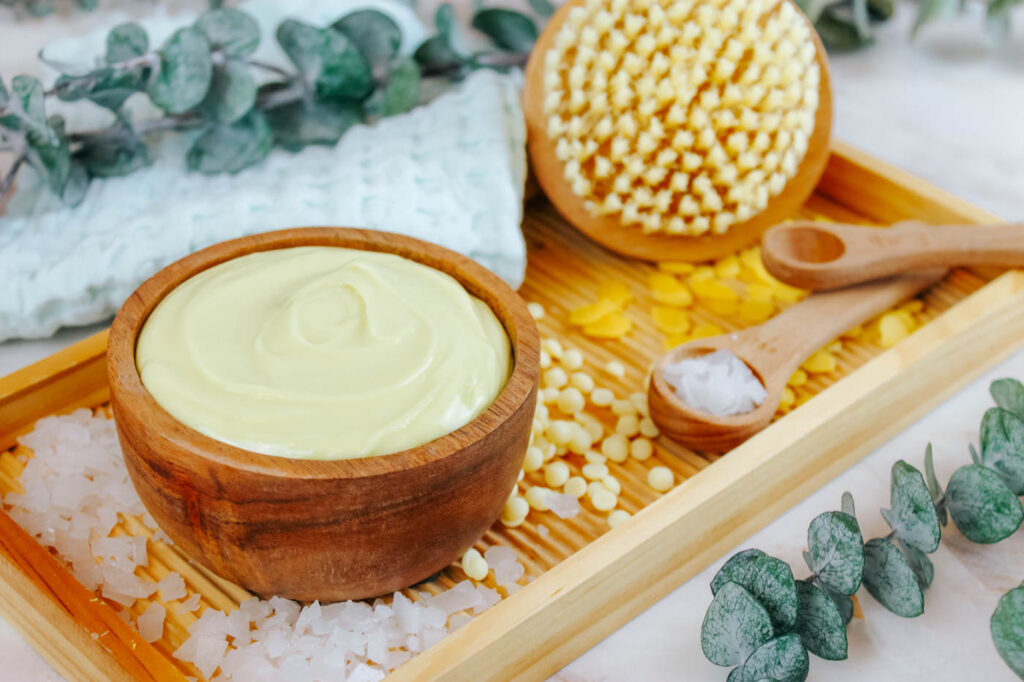 wooden bowl of magnesium lotion recipe sitting on a bath tray with cosmetic supplies