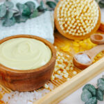 wooden bowl of magnesium lotion recipe sitting on a bath tray with cosmetic supplies