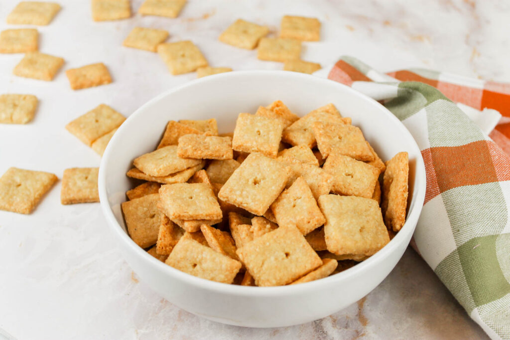 bowl of cheese crackers with fresh milled flour sitting on a countertop beside a checkered tea towel