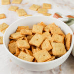bowl of cheese crackers with fresh milled flour sitting on a countertop beside a checkered tea towel
