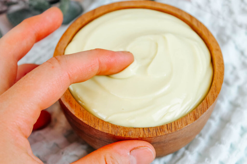 woman dipping her fingers into a bowl of magnesium lotion