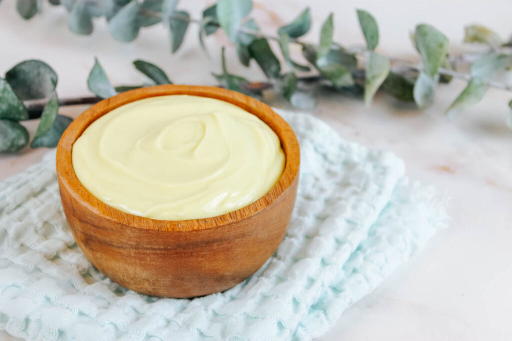 a small bowl filled with homemade lotion sits on a teal colored towel