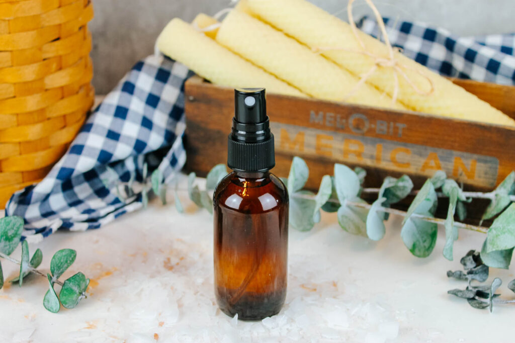 amber spray bottle sitting on a marble countertop next to some greenery and candles