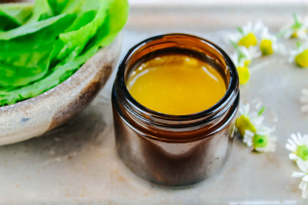 glass jar filled with healing balm sitting besides fresh cut herbs